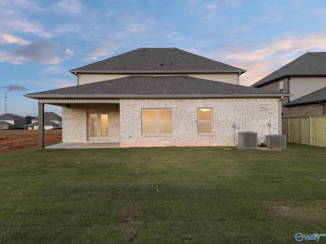 rear view of house with a patio area, central AC, a yard, fence, and a shingled roof