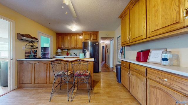 1303 7th Ave, Athens, AL 35611 - kitchen with freestanding refrigerator, brown cabinetry, light wood finished floors, light countertops, and a textured ceiling