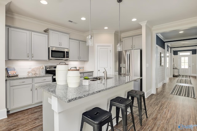 kitchen featuring stainless steel appliances, light stone counters, a center island with sink, and sink