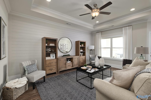 living room with a tray ceiling, ornamental molding, dark wood-type flooring, and ceiling fan