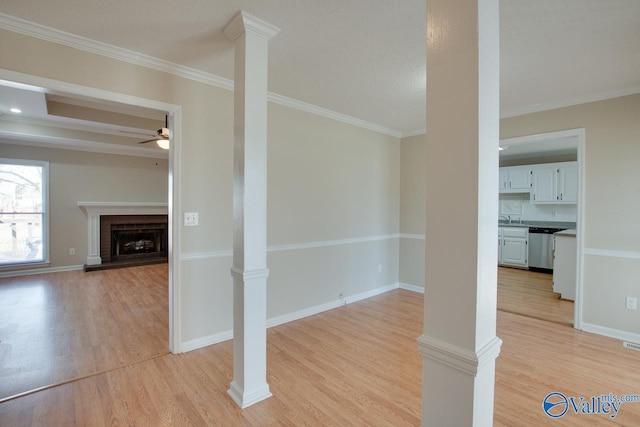 unfurnished dining area featuring ceiling fan, light wood-type flooring, a fireplace, and ornate columns