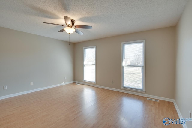 spare room with light wood-type flooring, a ceiling fan, visible vents, and a wealth of natural light