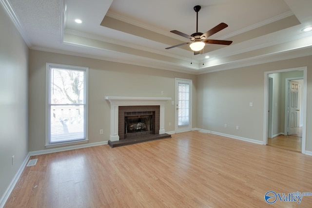 unfurnished living room featuring a healthy amount of sunlight, light wood-style flooring, a fireplace, and a raised ceiling