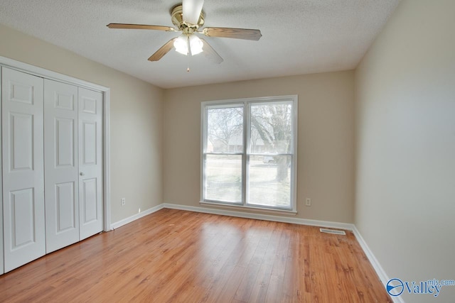 unfurnished bedroom with light wood-style floors, a closet, a textured ceiling, and baseboards