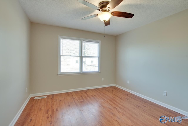 unfurnished room with baseboards, light wood-style flooring, visible vents, and a textured ceiling