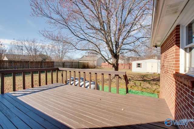 wooden deck with a fenced backyard, a storage unit, a lawn, and an outbuilding