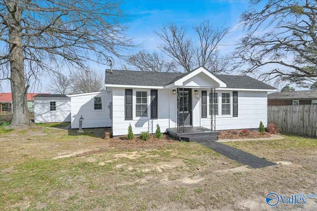 bungalow with a shingled roof, fence, and a front lawn