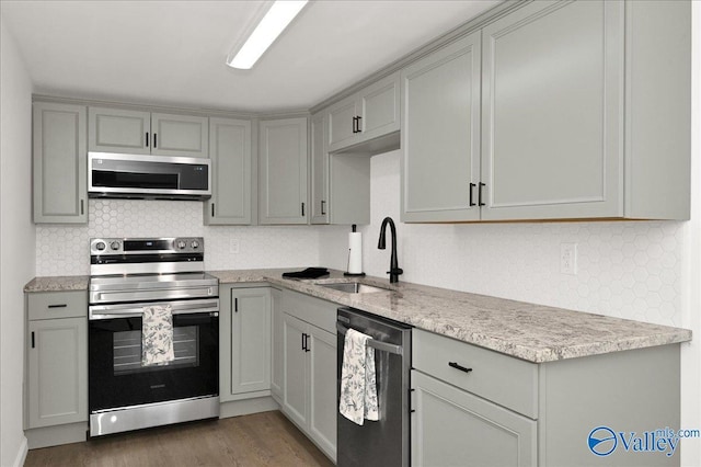 kitchen featuring appliances with stainless steel finishes, a sink, gray cabinetry, and wood finished floors
