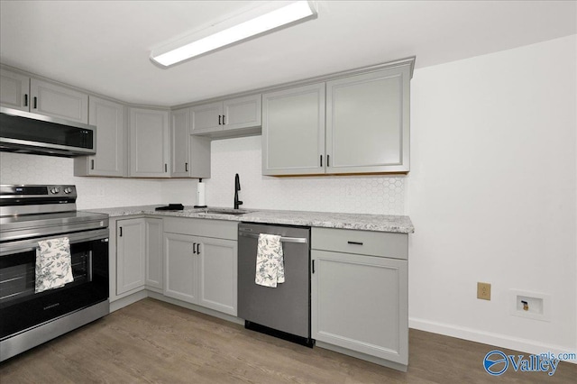 kitchen featuring decorative backsplash, appliances with stainless steel finishes, gray cabinets, light wood-style floors, and a sink