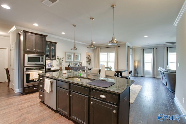 kitchen featuring appliances with stainless steel finishes, a center island with sink, light wood-type flooring, and a wealth of natural light