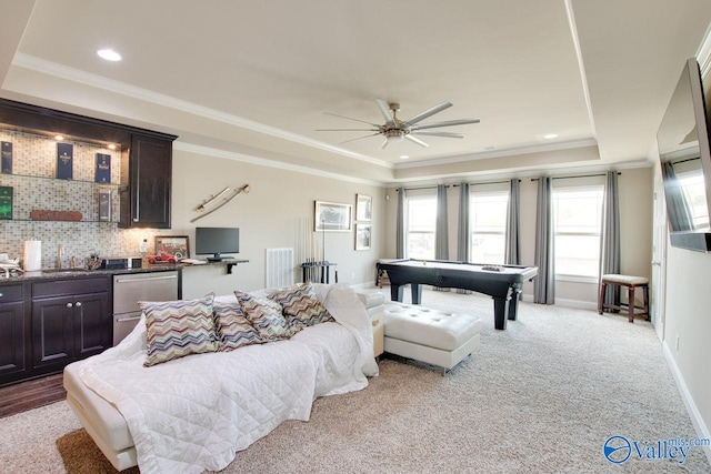 bedroom featuring indoor wet bar, ceiling fan, a tray ceiling, ornamental molding, and light colored carpet