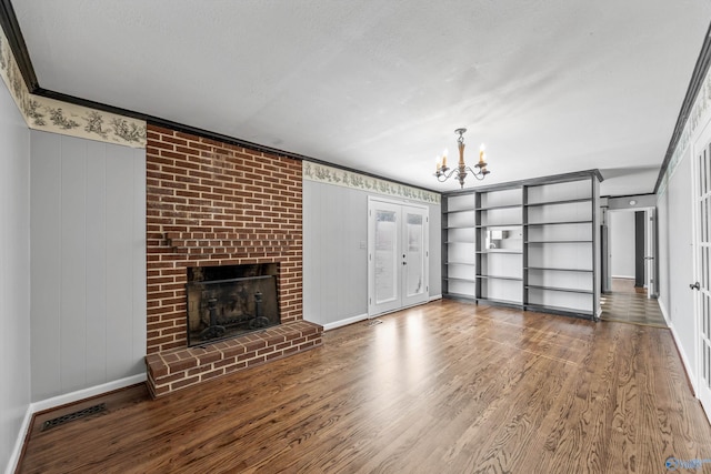 unfurnished living room featuring an inviting chandelier, crown molding, a brick fireplace, a textured ceiling, and wood-type flooring