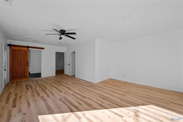 unfurnished bedroom featuring ceiling fan, a barn door, and light wood-type flooring