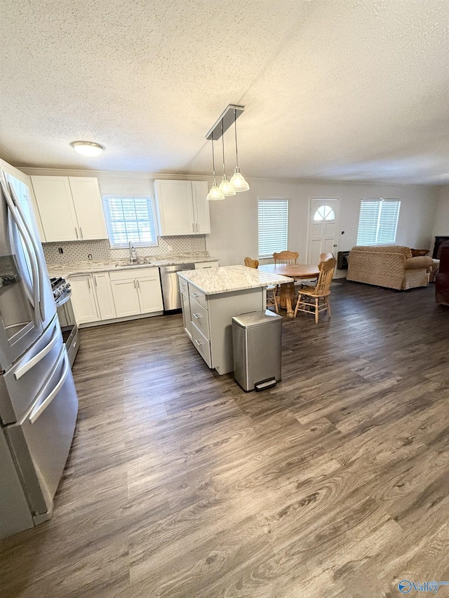 kitchen with appliances with stainless steel finishes, backsplash, decorative light fixtures, a center island, and white cabinetry