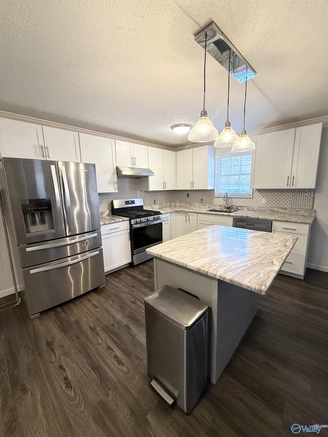 kitchen with hanging light fixtures, sink, appliances with stainless steel finishes, a kitchen island, and white cabinetry