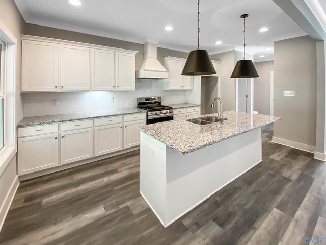 kitchen with stainless steel gas stove, custom exhaust hood, sink, a center island with sink, and white cabinets