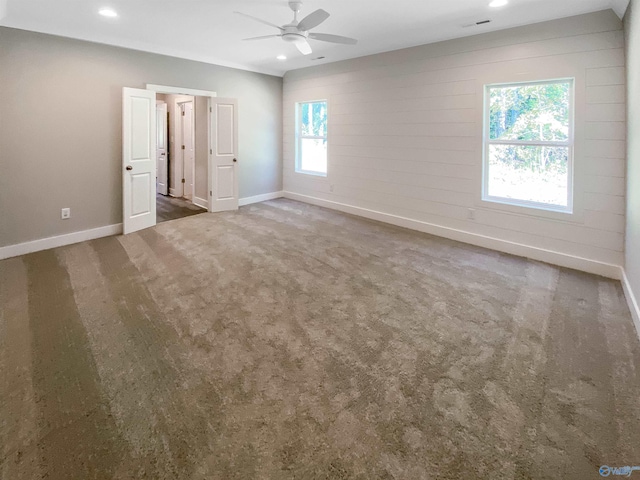 empty room featuring plenty of natural light, ceiling fan, and dark colored carpet