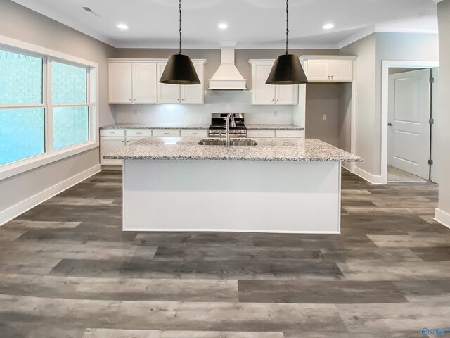 kitchen featuring light stone counters, custom exhaust hood, white cabinetry, sink, and a kitchen island with sink