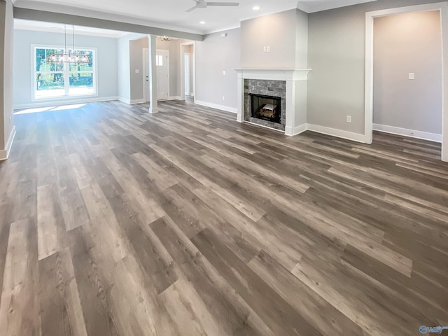 unfurnished living room featuring ceiling fan with notable chandelier, dark hardwood / wood-style flooring, and a stone fireplace