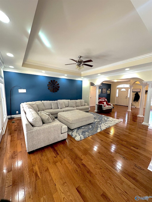 living room featuring ornate columns, hardwood / wood-style flooring, ceiling fan, a raised ceiling, and crown molding