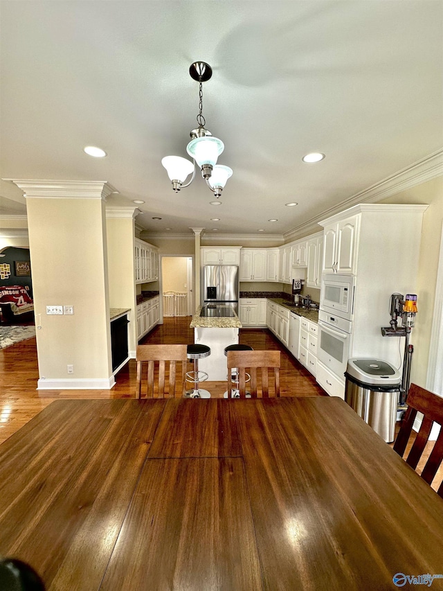 kitchen featuring white cabinetry, a breakfast bar area, a notable chandelier, crown molding, and white appliances