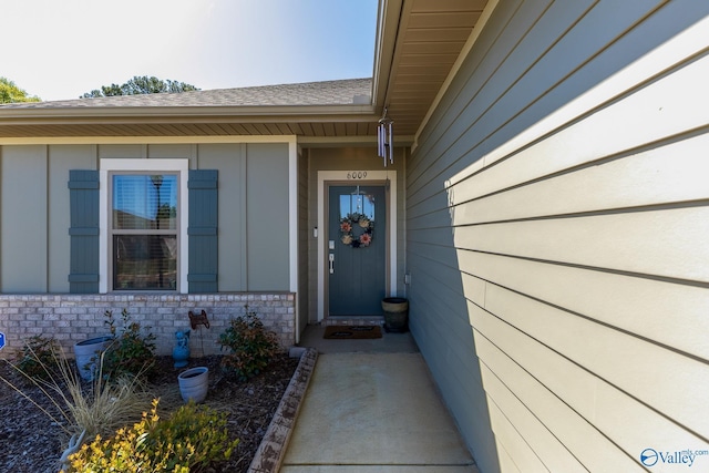 view of exterior entry featuring board and batten siding and roof with shingles