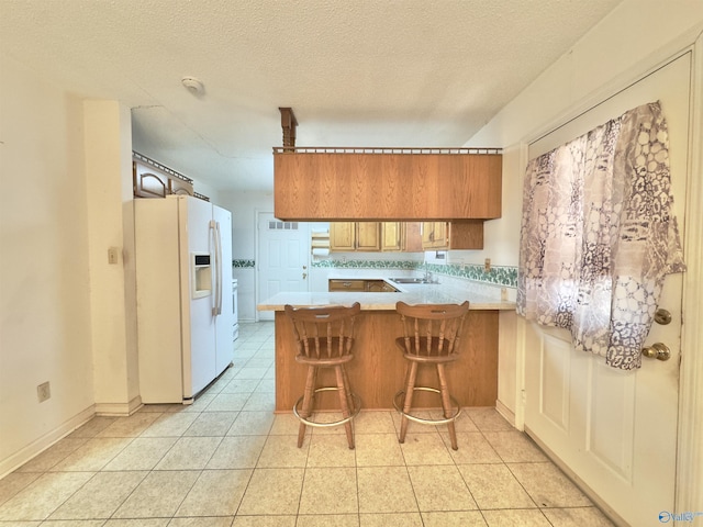 kitchen with white fridge with ice dispenser, sink, kitchen peninsula, a textured ceiling, and a breakfast bar area