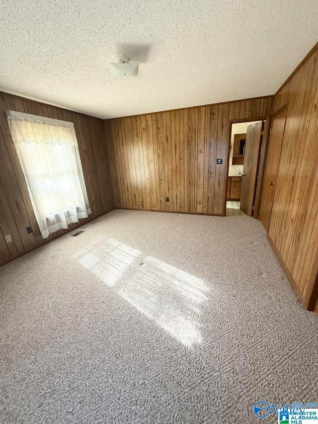 carpeted empty room with wooden walls and a textured ceiling