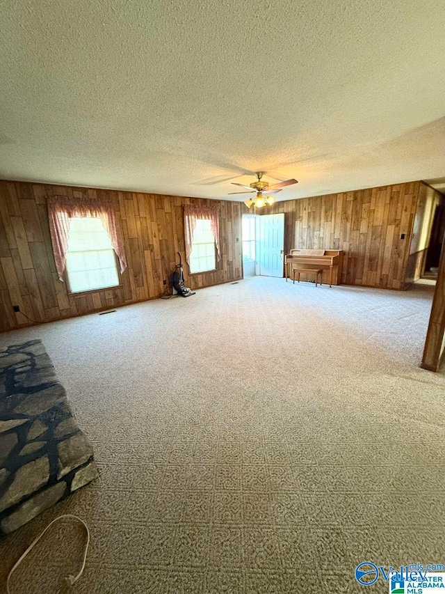 interior space featuring ceiling fan, carpet flooring, a textured ceiling, and wood walls