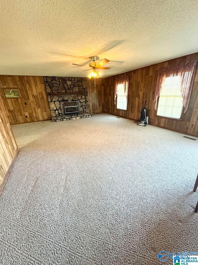 unfurnished living room with ceiling fan, a textured ceiling, and wood walls