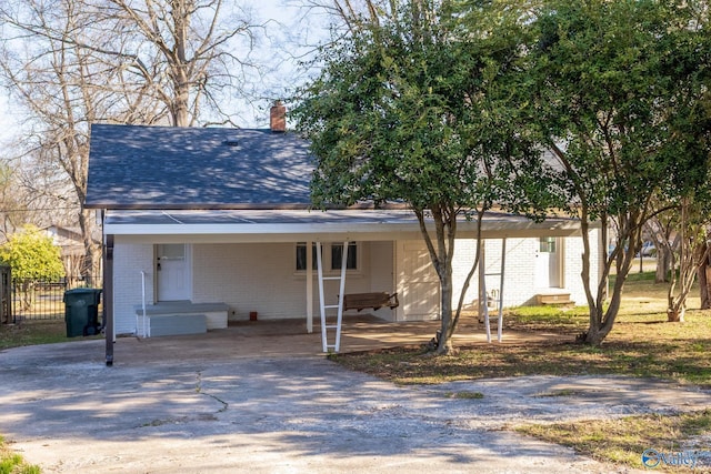 view of front facade with brick siding, entry steps, concrete driveway, an attached carport, and a chimney