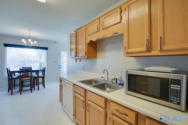 kitchen with stainless steel microwave, white dishwasher, light countertops, a chandelier, and a sink