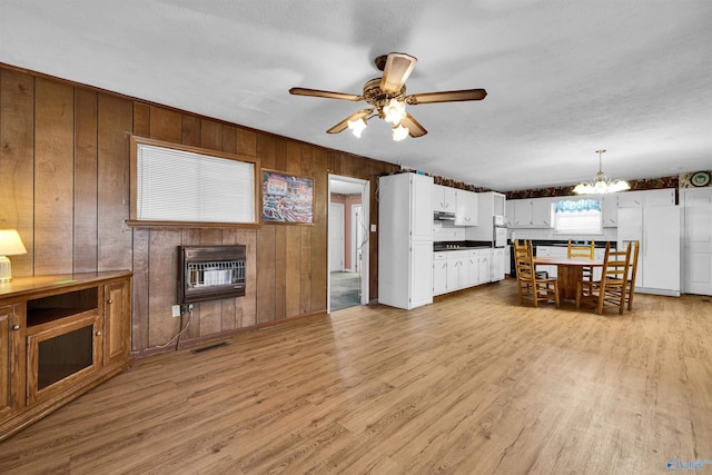 living area with light wood finished floors, heating unit, visible vents, a fireplace, and ceiling fan with notable chandelier