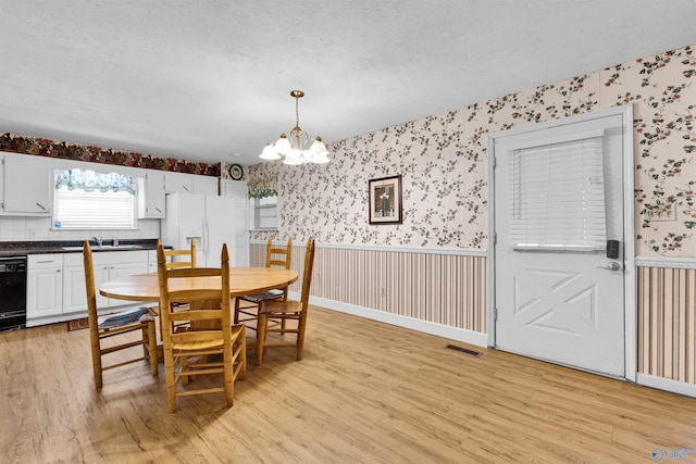 dining room with a wainscoted wall, light wood-type flooring, visible vents, a chandelier, and wallpapered walls