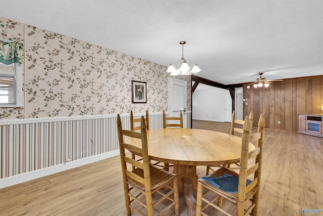 dining room featuring wallpapered walls, light wood finished floors, and ceiling fan with notable chandelier