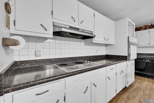 kitchen with black appliances, white cabinetry, light wood-style flooring, backsplash, and under cabinet range hood