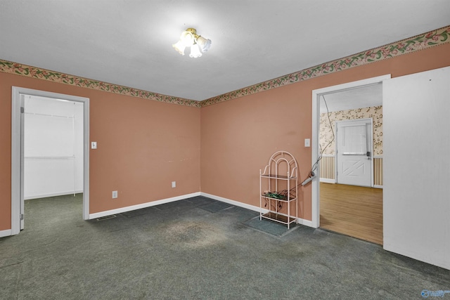 empty room with wallpapered walls, dark colored carpet, and baseboards