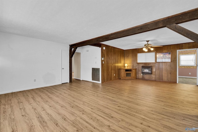 unfurnished living room with wooden walls, wood finished floors, beamed ceiling, baseboards, and ceiling fan