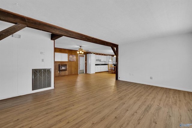 unfurnished living room with light wood-style flooring, ceiling fan, beamed ceiling, a fireplace, and visible vents
