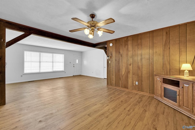 unfurnished living room with wood walls, baseboards, light wood-style floors, and ceiling fan