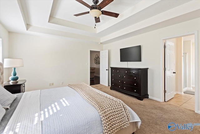 carpeted bedroom featuring a raised ceiling, connected bathroom, and ceiling fan