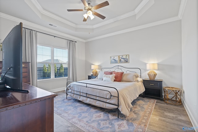 bedroom featuring ornamental molding, hardwood / wood-style floors, ceiling fan, and a tray ceiling