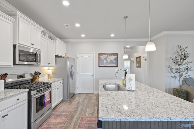 kitchen featuring pendant lighting, sink, white cabinets, stainless steel appliances, and a center island with sink