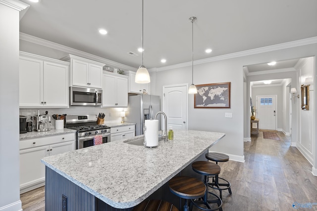 kitchen with pendant lighting, white cabinetry, stainless steel appliances, an island with sink, and a kitchen bar