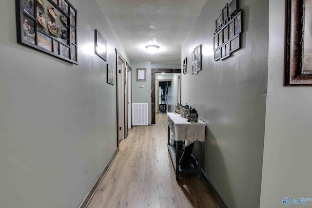 hall featuring light wood-type flooring and a textured ceiling