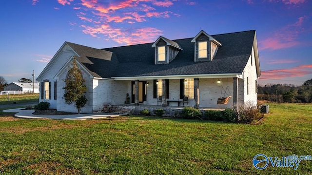 cape cod home featuring covered porch and a lawn