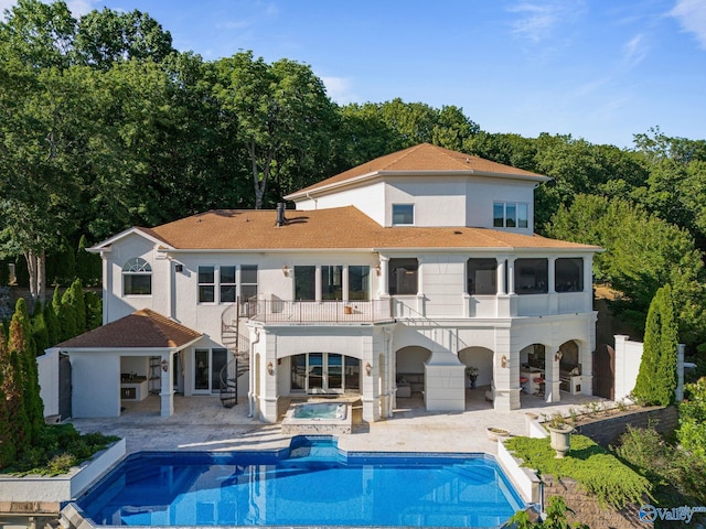 rear view of house with a balcony, a swimming pool with hot tub, and a patio