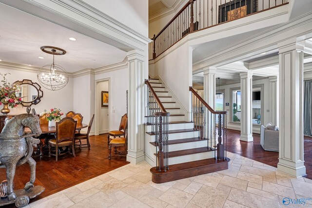 stairs featuring ornate columns, crown molding, wood-type flooring, and a notable chandelier