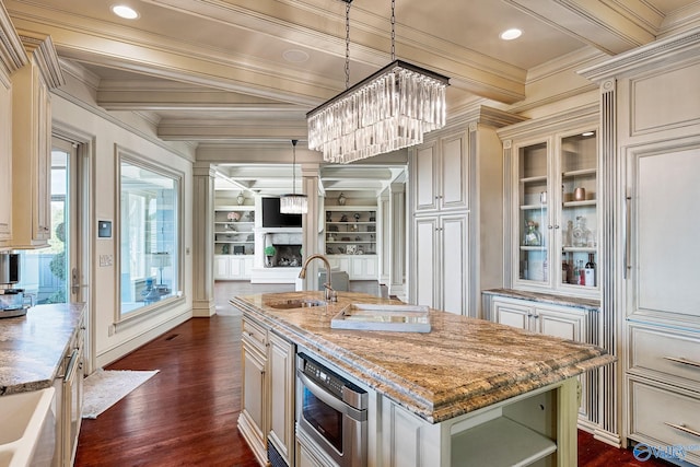 kitchen featuring sink, hanging light fixtures, ornamental molding, an island with sink, and light stone countertops