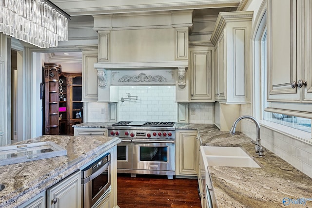 kitchen with sink, light stone countertops, cream cabinets, and range with two ovens